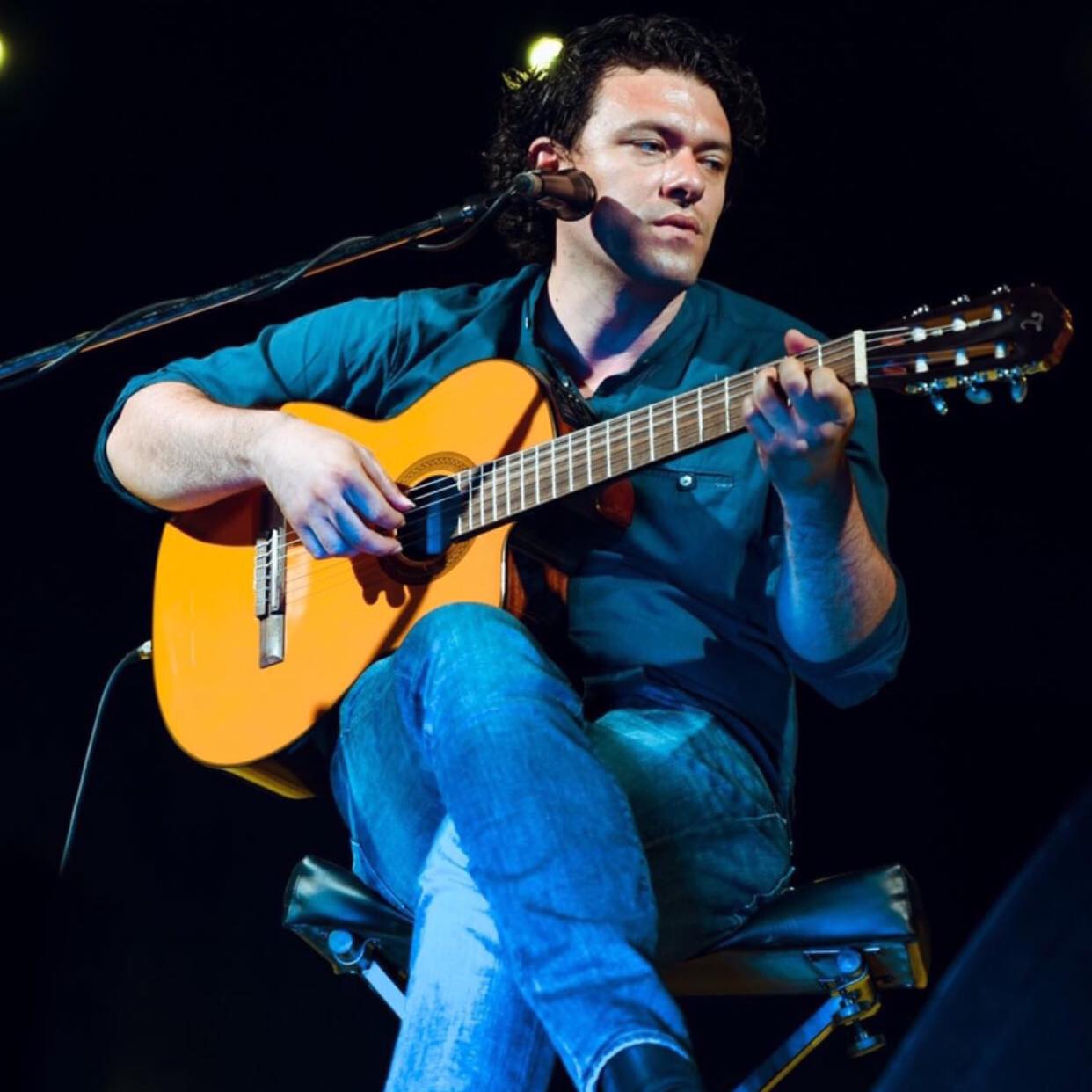 Un uomo su una sedia che suona una chitarra acustica.